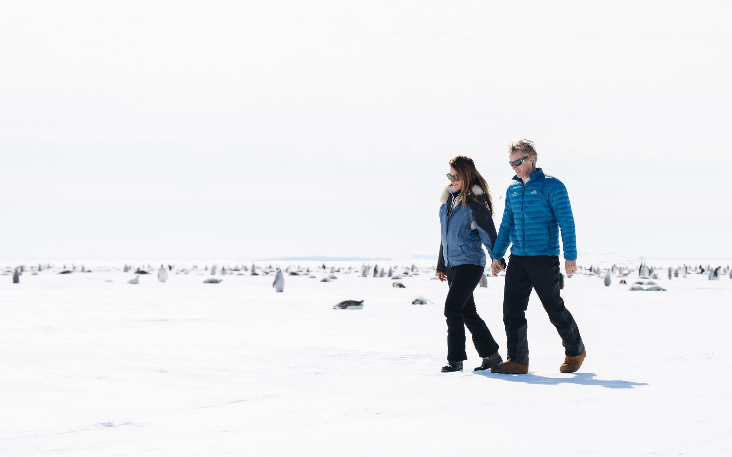man and woman holding hand walking across the Antarctic tundra