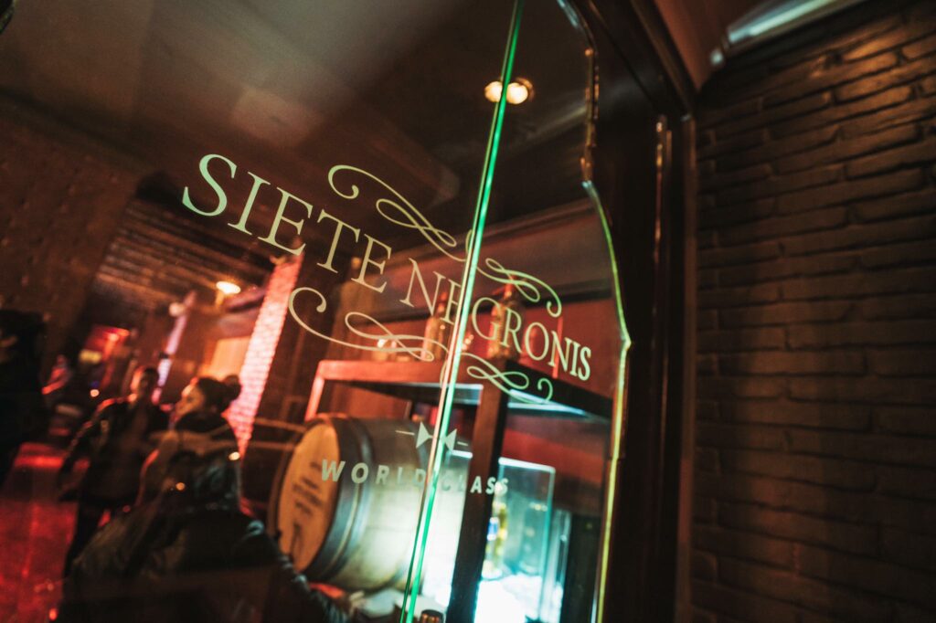 A close up of the Siete Negronis logo  sign on the window of Siete Negronis Bar. 