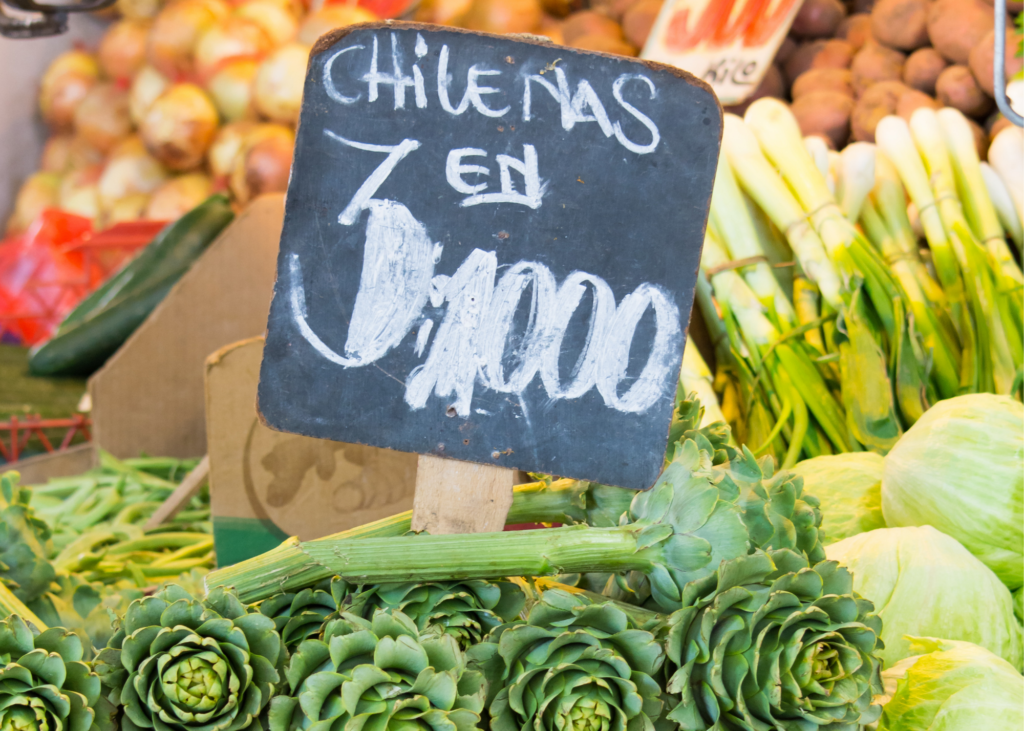 Close up of an open market sign displaying the cost of the artichokes that sit under it. 