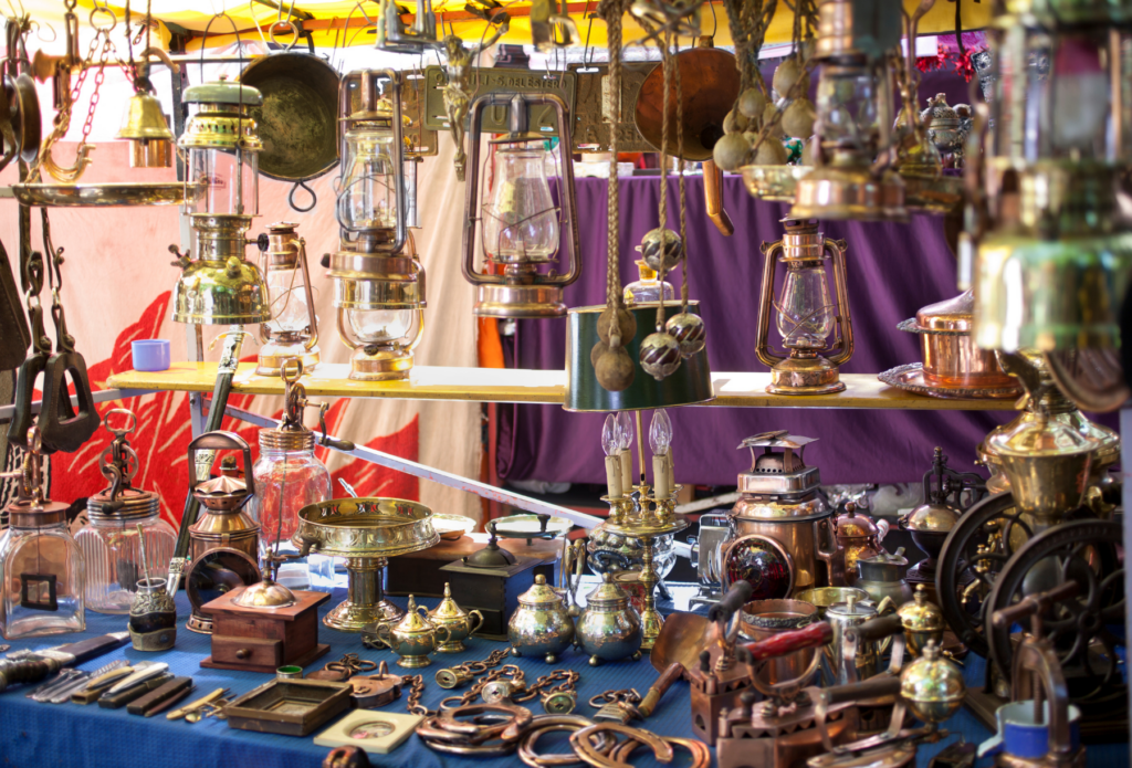 Colorful outdoor market table with an array of objects spread out on the table as well as objects such as lanterns hanging above.  