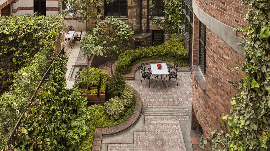 a patio with a table and chairs surrounded by greenery.