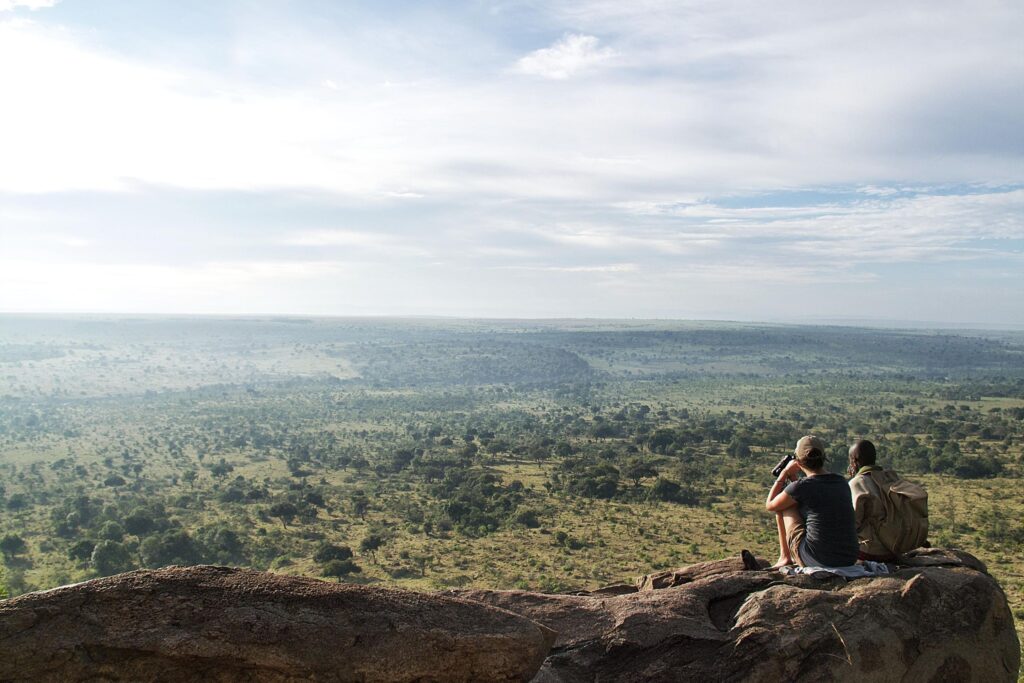 two people sitting on a rock in front of a plain in ngare serain, kenya