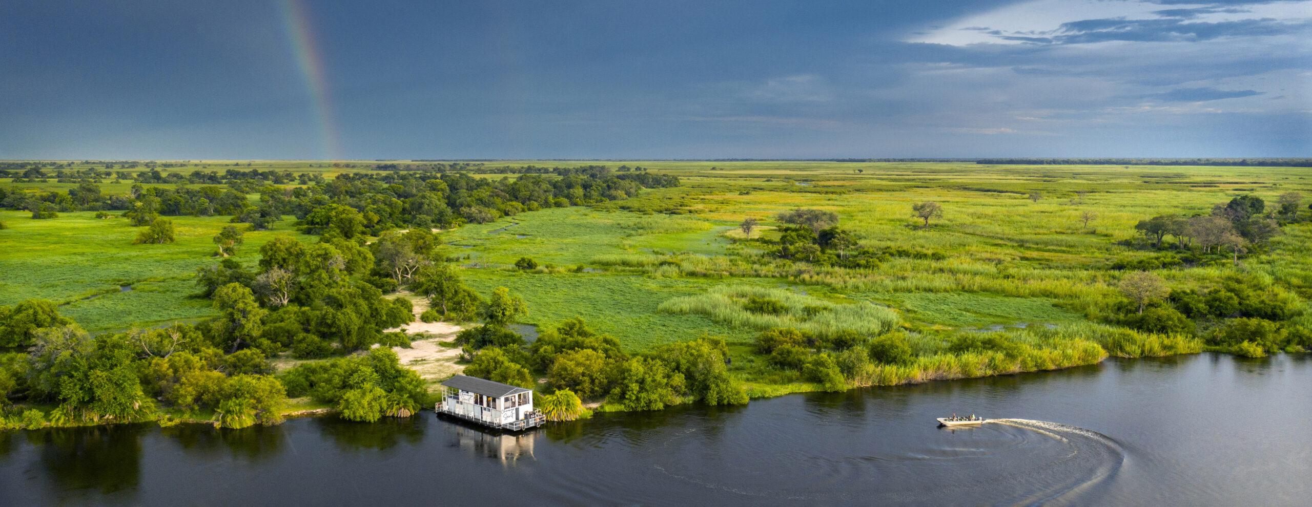 The lush Okavango Delta radiates in shades of green backdropped by a moody, rainbow-crowned sky. Image courtesy of Natural Selection.