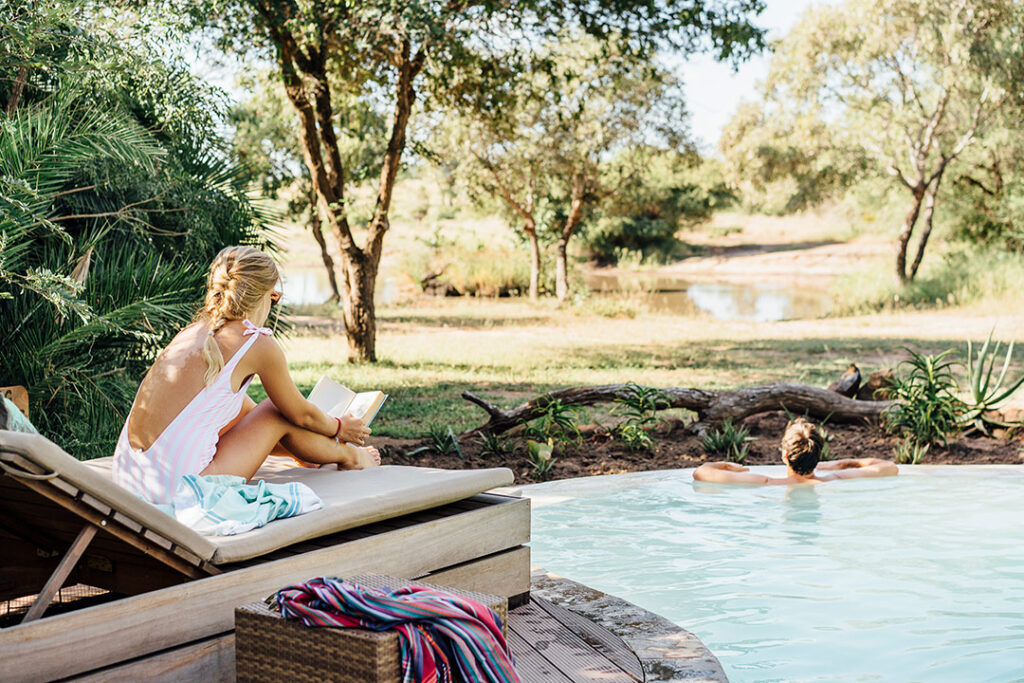 A woman relaxes at Tanda Tula Safari Camp where the pool looks upon a river bed.