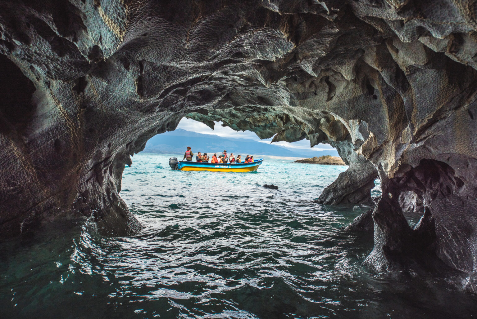 View through the marble caves to a small boat in the water with passengers in orange lifejackets