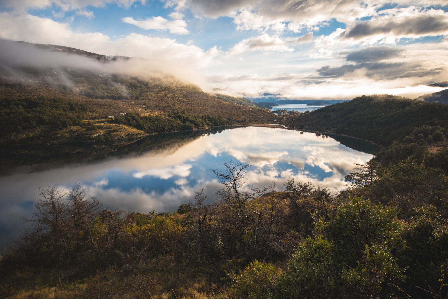 Patagonian lake surrounded by hills with clouds mirroring on the water