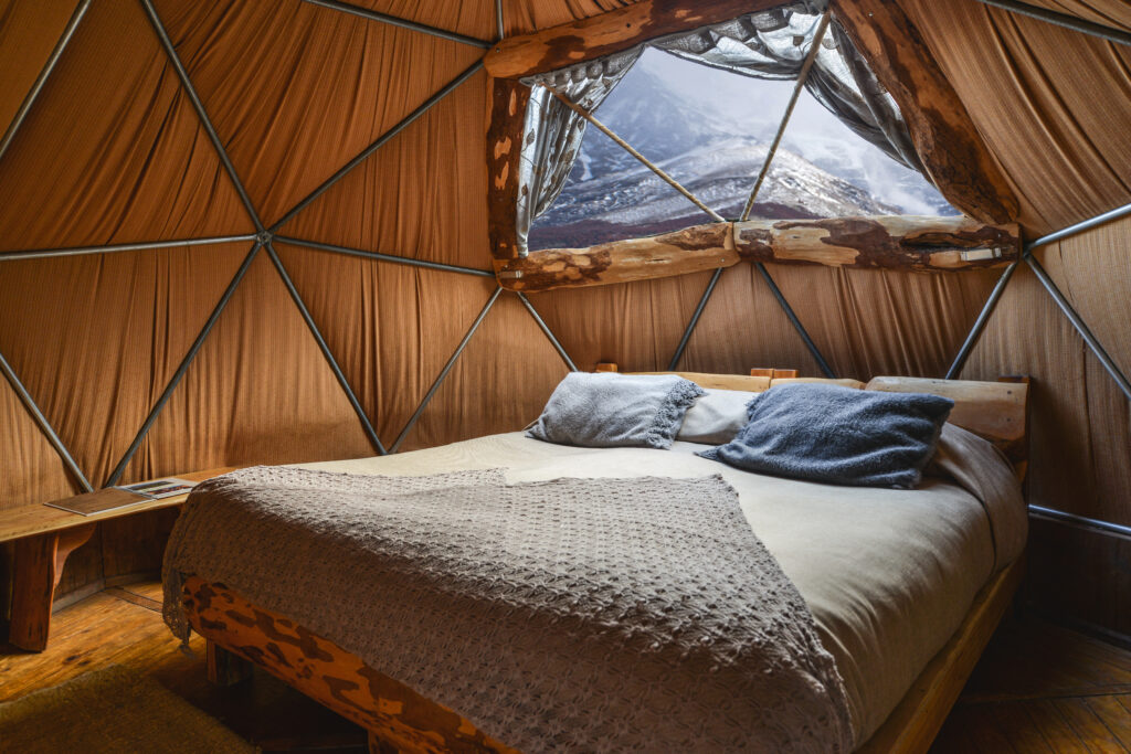 Interior of a standard dome with a made bed and a window to the mountains