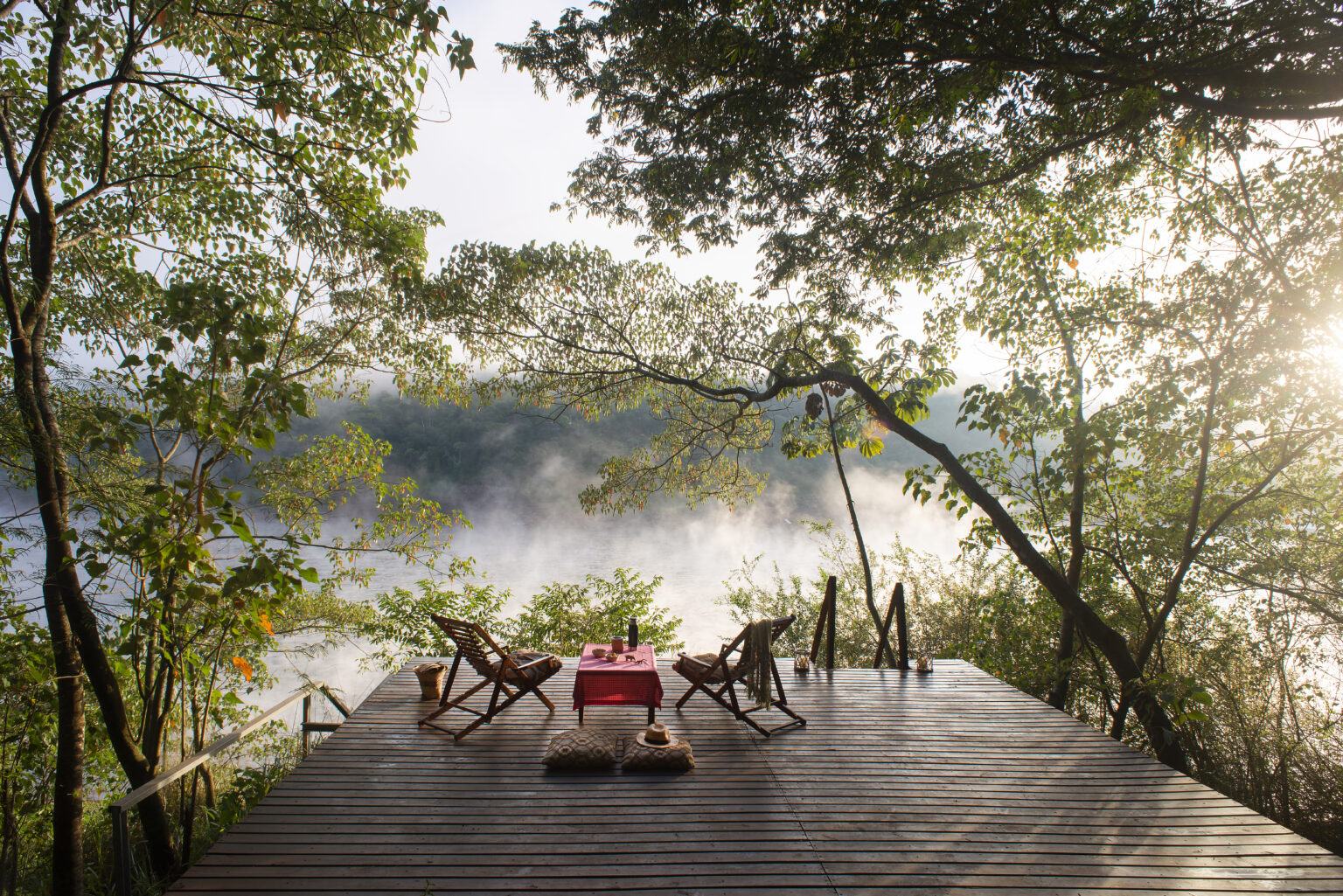Two chairs and a table on a deck overlooking foggy jungle