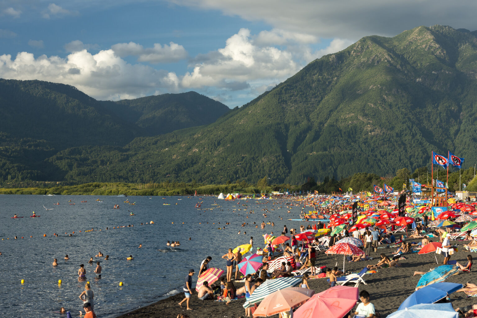 swimmers on the beach of Lake Villarrica with colorful umbrellas in front of a mountain range