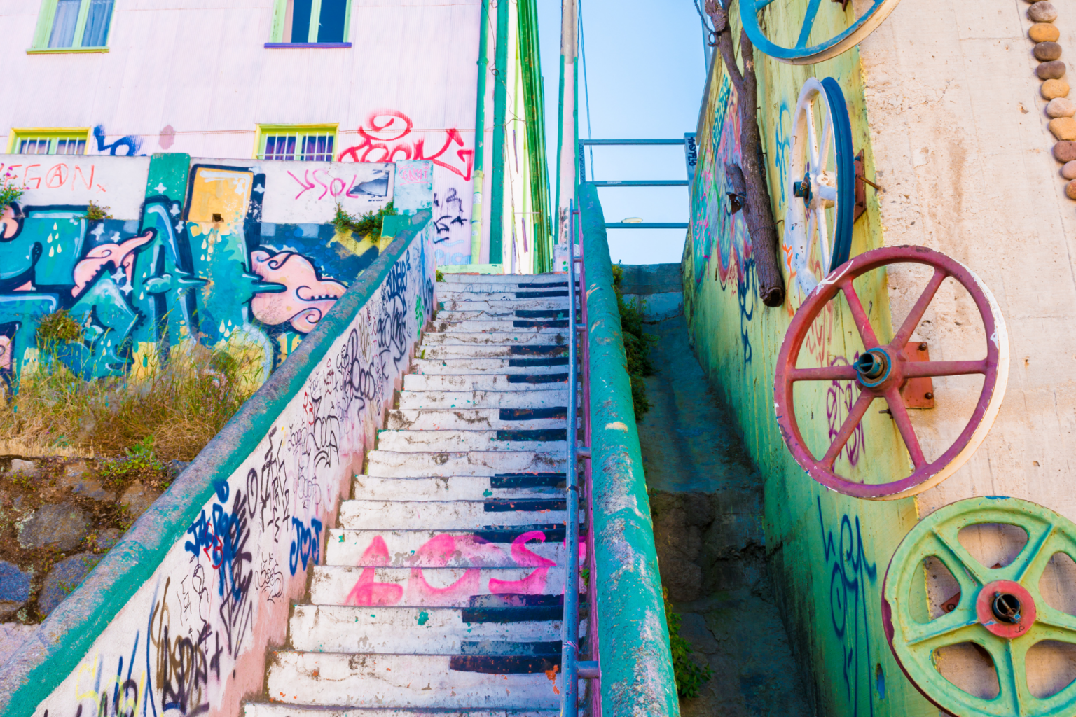 Looking up at colorful outdoor stairs painted like piano keys, with graffiti art on the surrounding buildings