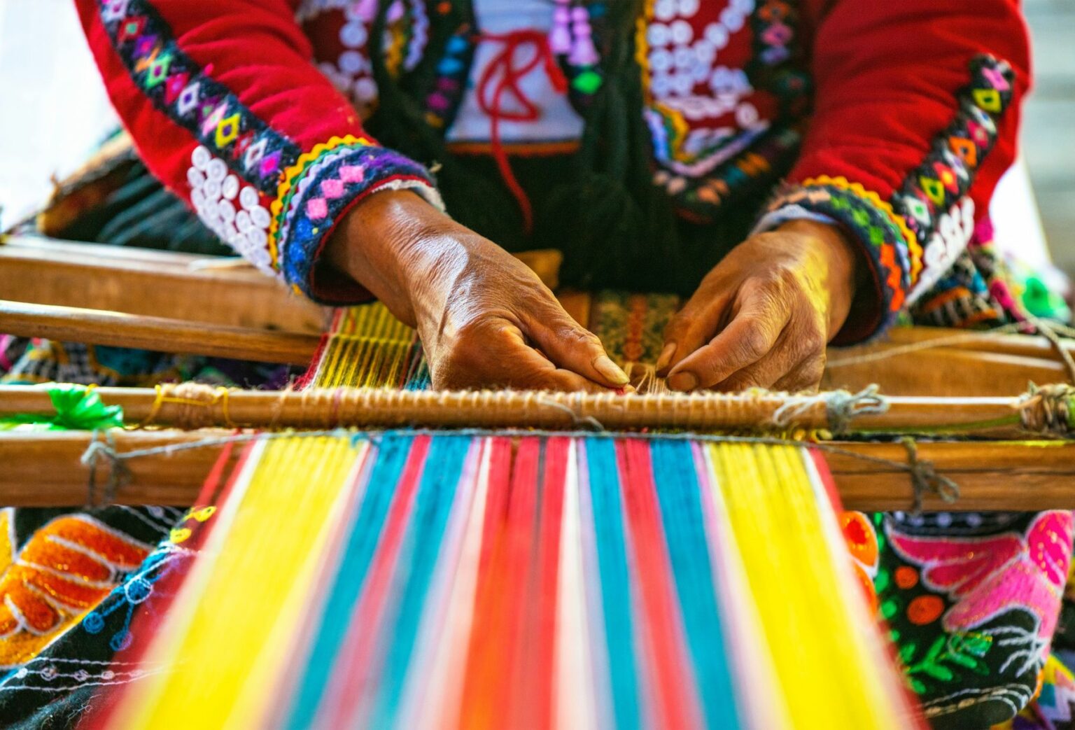 Hands of woman in bright clothing weaving colorful tapestry