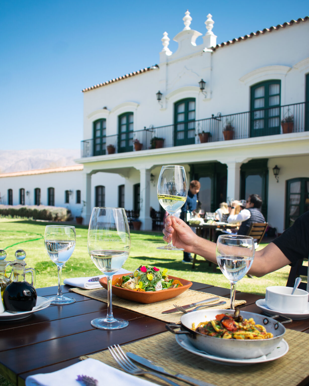 Table with wine glasses and food in front of white building