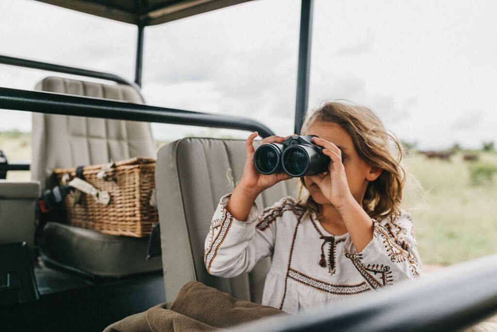 A young girl looking through a pair of binoculars on safari.