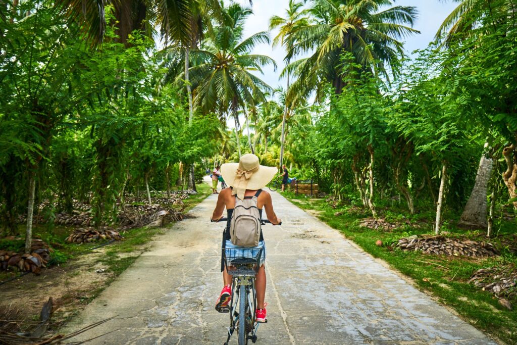 Visitor cycling past verdant palms on La Digue, a serene highlight in our Seychelles island travel guide, perfect for secluded beach adventures.