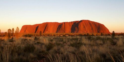 Uluru commands the landscape, bright red at sunset
