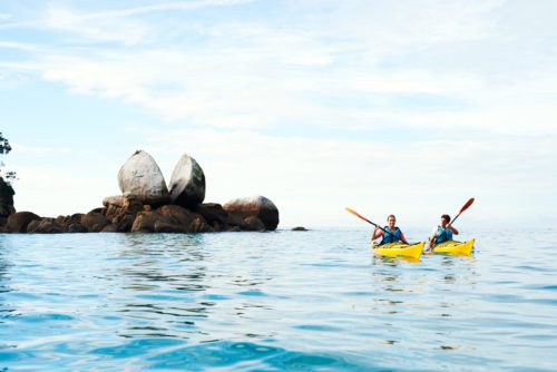 Two kayakers paddle toward Split Apple Rock in Abel Tasman National Park on New Zealand safari