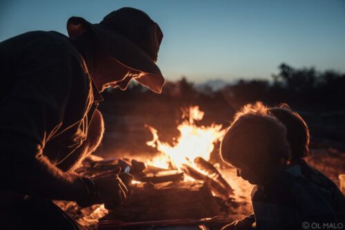 man and boy leaning over a fire at night while they visit kenya