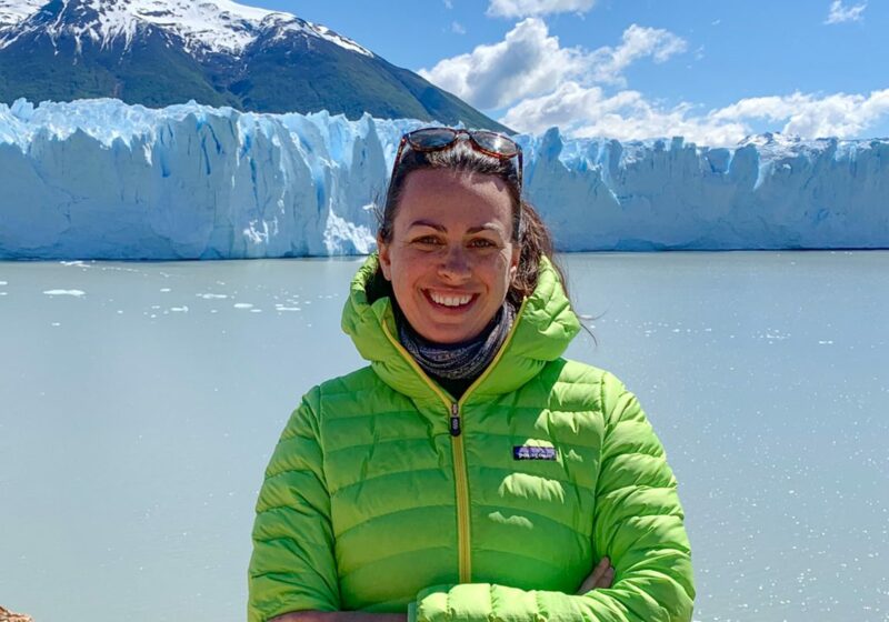 A woman in a green jacket standing in front of a glacier.