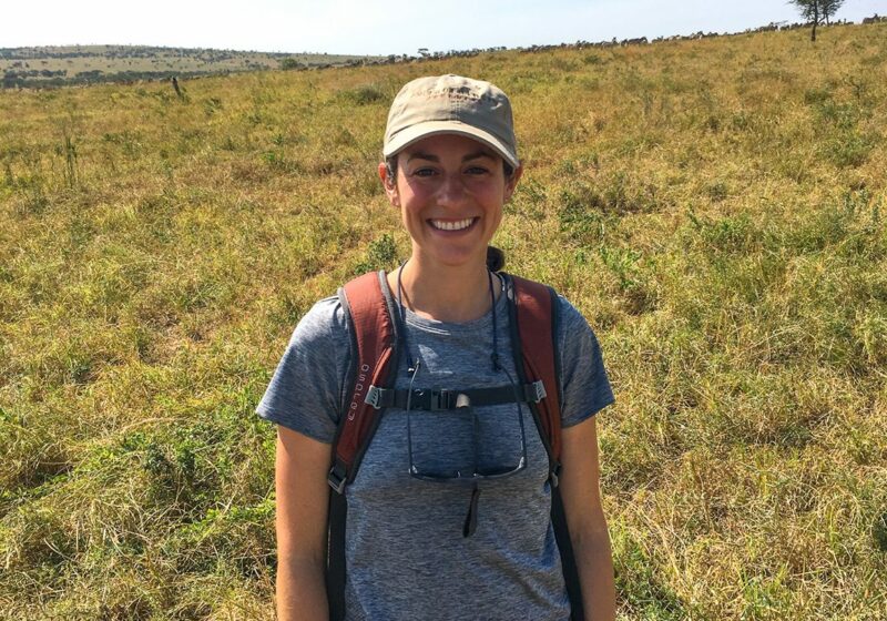 A woman standing in a field with a backpack.