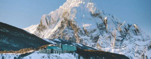 Modern hotel on hill in front of towering snow capped mountain