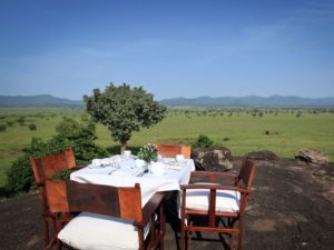 outside lunch table with white linens set up on a rocky outcropping overlooking the green savannah in Kidepo Valley